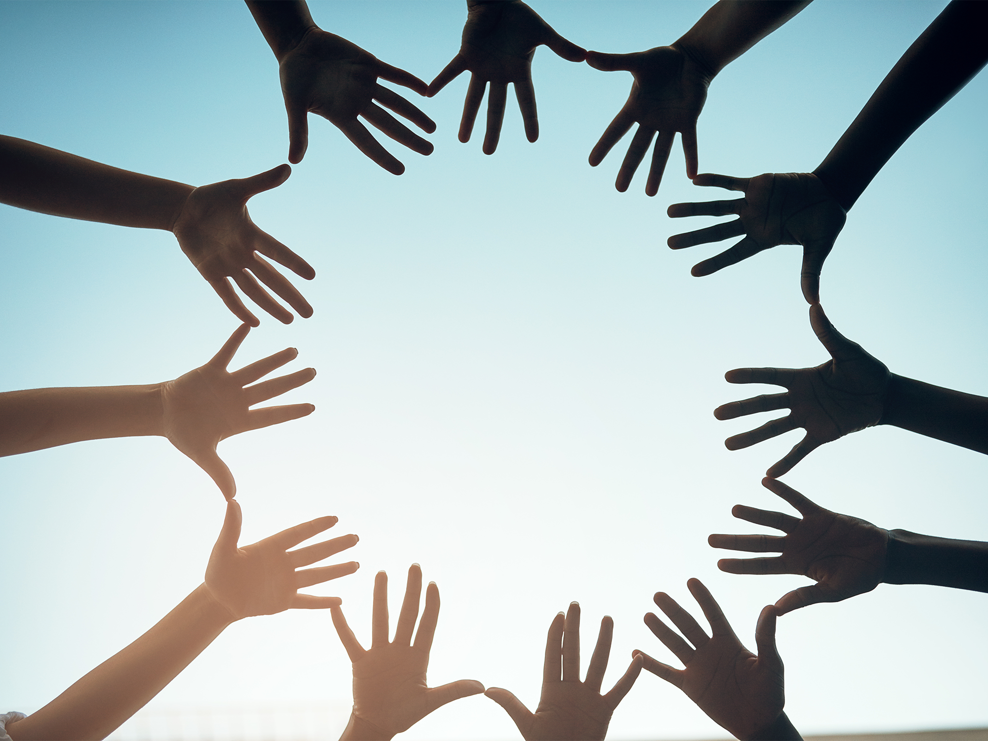 A circle of hands silhouetted against the sunlight