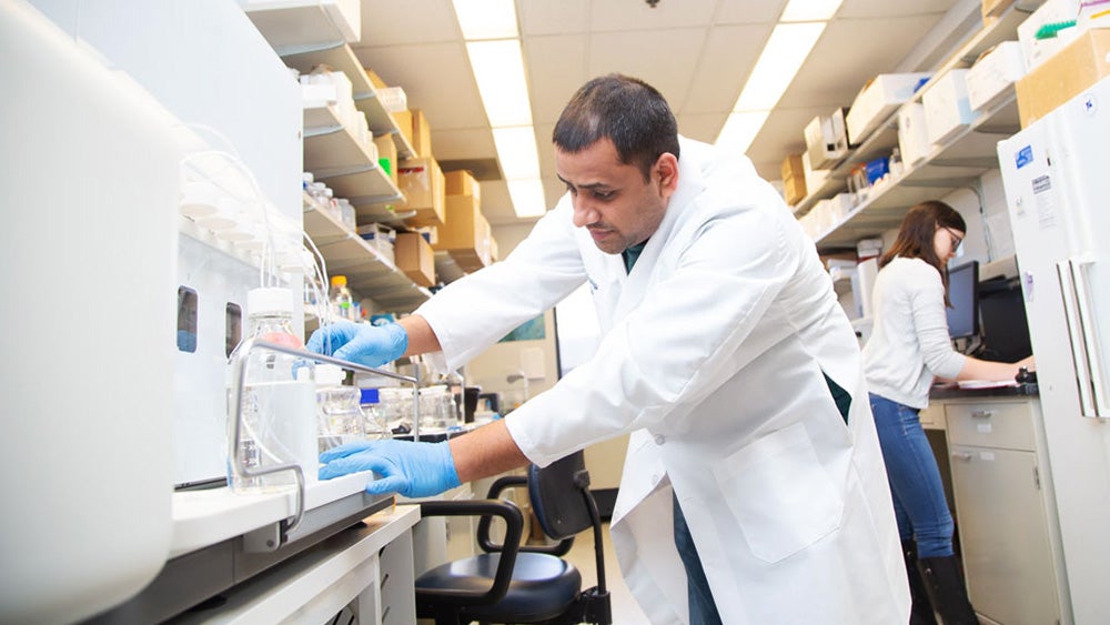 A lab worker draws liquid from a tank into a vial in the laboratory