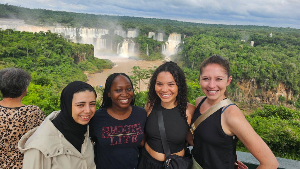 Four women stand together with Iguazu Falls in the background