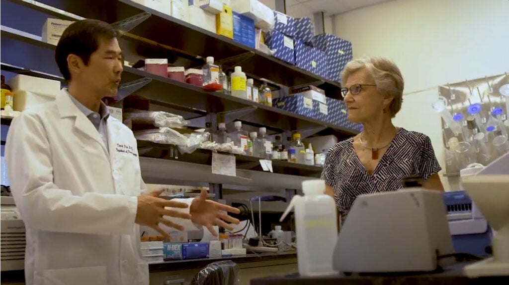 A woman looks at a researcher in white lab coat as he speaks