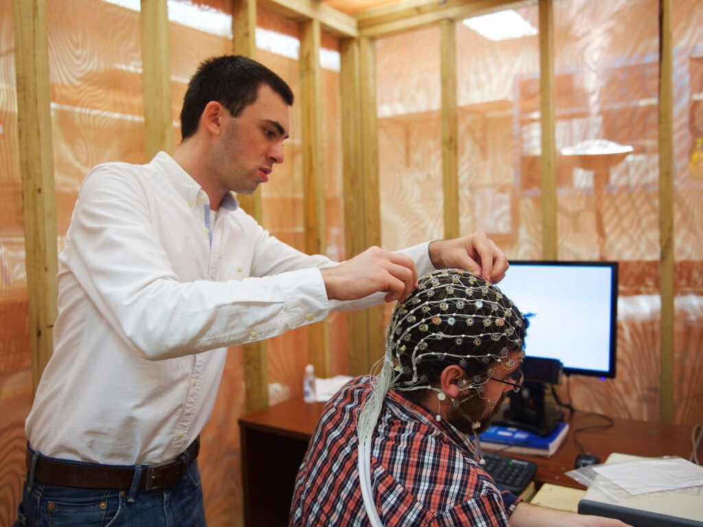 A researcher fastens a cap of electrodes to the head of a volunteer